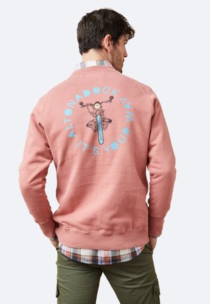 Sudadera de color rosa claro con un gráfico de una bicicleta en la parte posterior, con texto azul que dice "ALTONADOCK AVM IT'S YOUR." Puños y dobladillo de canalé.