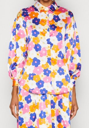Pitkähihainen napitettava paita, jossa on vaaleanpunainen, oranssi, sininen ja valkoinen kukkakuosi, käytettynä yhdessä samanmallisen hameen tai housujen kanssa.