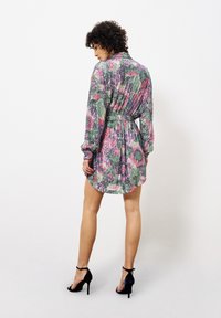 Blumenmuster-Kleid mit langen Ärmeln, taillierter Taille und Kragen. Das Material hat eine strukturierte Oberfläche. Kombiniert mit schwarzen High-Heels.