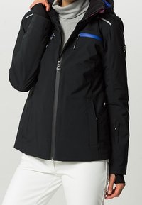 Svart vattentät jacka med dragkedja fram, blå akcent, flera fickor och en huva med strukturerad insida. Slät, elegant tyg.