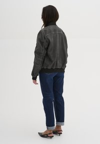 Gray leather bomber jacket with ribbed cuffs and hem, featuring gathered side detailing. Worn with dark denim jeans and black pointy shoes.