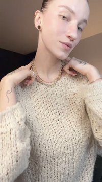 Camisola de malha bege com corte solto, colar de corrente dourada e prateada em camadas com vários formatos de elos, usado sobre pele clara.