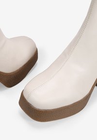 Bottes blanches à la cheville avec un bout arrondi, un upper en cuir lisse et une semelle plateformée texturée marron. Design épuré avec des accents de couture subtils.