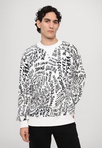 White sweatshirt with black text and patterns, featuring round neck and ribbed cuffs. Designed with a relaxed fit and visual emphasis on branding.