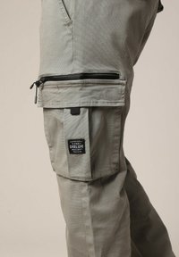 Grijze cargobroek gemaakt van duurzaam materiaal, met rits- en opgestikte zakken, voorzien van een geweven label met de merknaam.