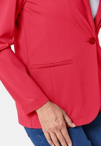 Rode stoffen blazer met een enkele knoopsluiting, gestructureerde revers en een zijzak, met een gladde textuur en een getailleerde pasvorm.