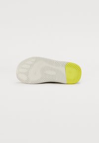 Talpa elegantă de pantof sport din cauciuc alb, cu striații texturate, având un accent galben vibrant pe călcâi pentru o aderență sporită.