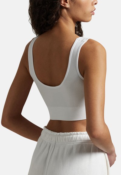 Bílý žebrovaný crop top se širokými ramínky, kulatým zády a bezešvou páskou. Kombinován s lehce barevnými tepláky s elastickým pasem.