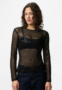 Crna majica dugih rukava od prozirnog materijala, ukrašena šljokicama. Ima četvrtasti izrez i tanke manšete. Strukturni kroj.