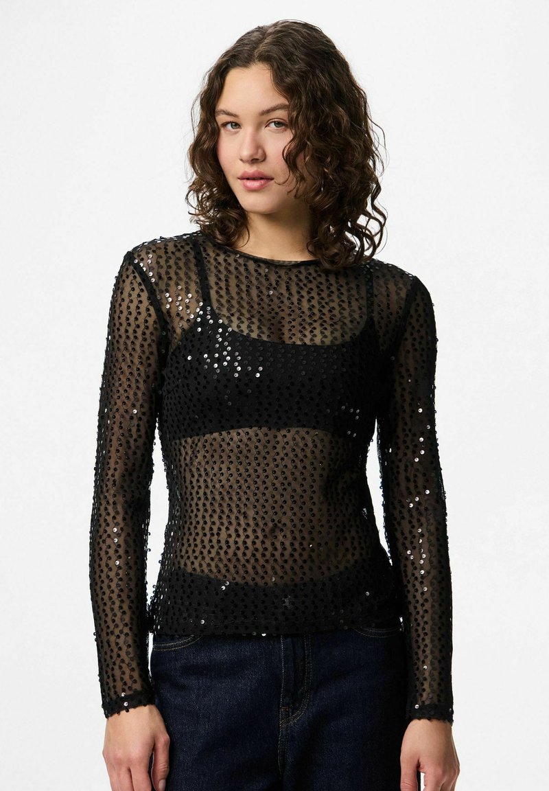 Crna majica dugih rukava od prozirnog materijala, ukrašena šljokicama. Ima četvrtasti izrez i tanke manšete. Strukturni kroj.