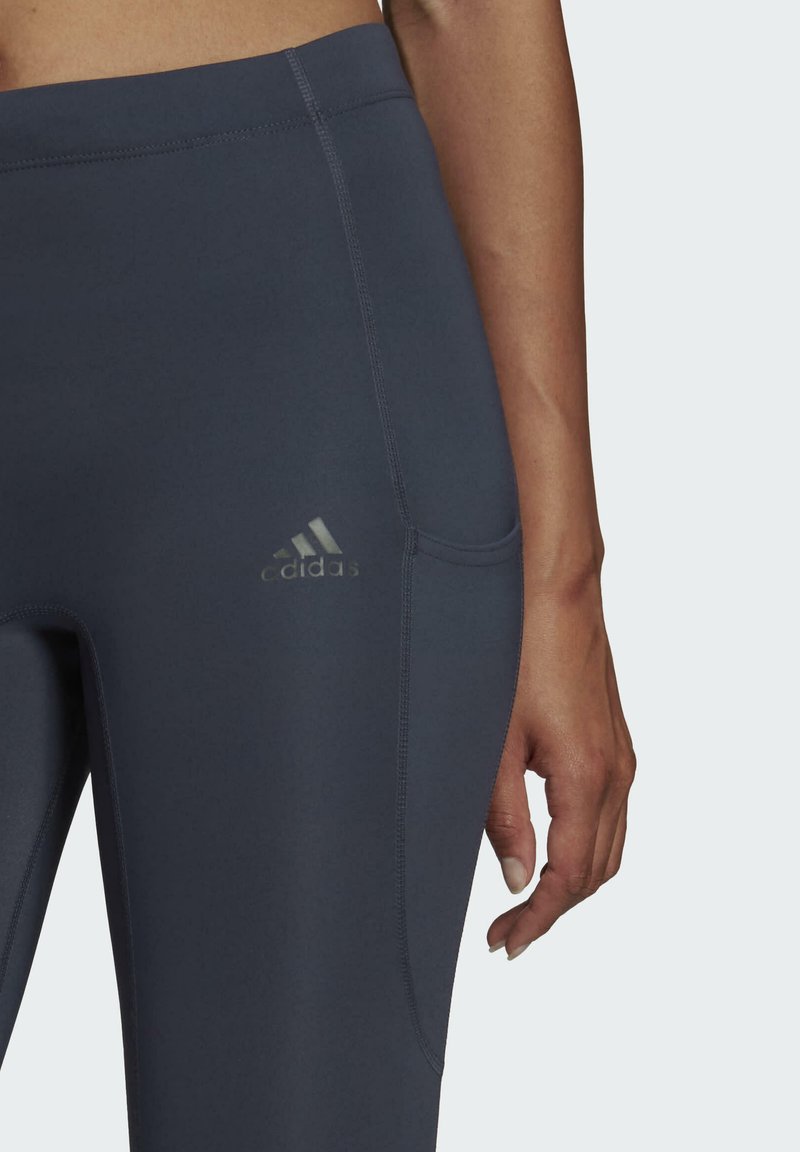 Adidas donkergrijze leggings met een soepele, rekbare textuur, voorzien van een zichtbare zak en het logo in reflectief zilver nabij de heup.