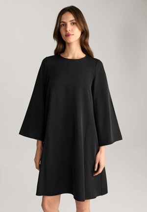 Schwarzes Kleid mit lockerer Passform, rundem Ausschnitt und weit ausgestellten Ärmeln. Hergestellt aus glattem Stoff mit geradem Saum. Einfaches Design.