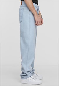 Heledad sinised, laiad teksapüksid, millel on sile tekstuur ja tagataskud. Kombineeritud mustade aktsentidega valgete sporditossudega.