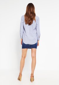 Randig skjorta i blått och vitt, bakvy, kombinerad med en denimkort kjol och bruna klackar med remmar, avslappnad passform med uppvikt ärmar.