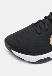 Černé atletické tenisky s síťovaným svrchním materiálem, gumovou podešví a bílými akcenty. Mají strukturovaný povrch a detail loga v růžovém zlatu.