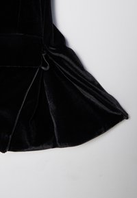 Tissu en velours noir avec une fermeture éclair partiellement ouverte dévoilant la texture et les plis sur un fond gris clair.