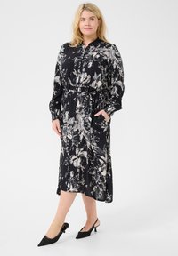 Zwarte bloemen midi-jurk met lange mouwen, knoopsluiting, cinched taille en zijzakken. Gecombineerd met zwarte slingback hakken.