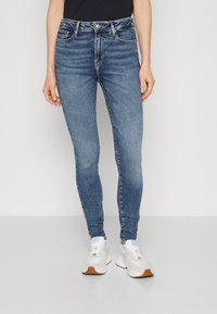 Smala jeans i medelblå denim, med fem fickor, en knappgylft stängning och lätt blekta områden för textur. Samman med vita sneakers.