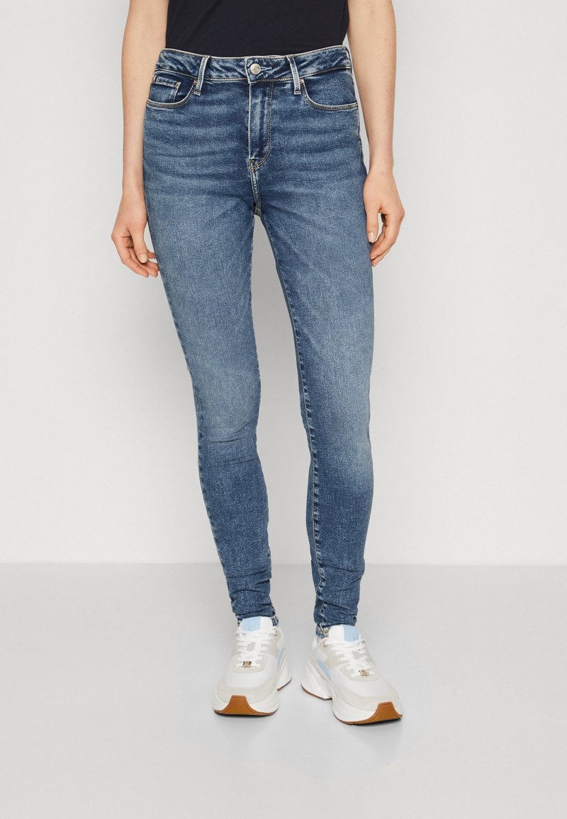 Smala jeans i medelblå denim, med fem fickor, en knappgylft stängning och lätt blekta områden för textur. Samman med vita sneakers.