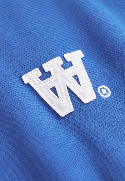 Tela azul con una superficie texturizada, que presenta un gran logotipo bordado en blanco con la letra "W" y un pequeño símbolo de marca registrada en blanco.