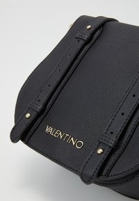 Borsa a mano in pelle nera con finitura testurizzata, hardware in tonalità dorata e logo 'VALENTINO'. Presenta tracolle regolabili e un design snello e compatto.