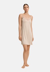 Vestido de tirantes en beige claro, hecho de una tela suave. Presenta tirantes finos y detalles de encaje alrededor del escote. Diseño sencillo, hasta la rodilla.