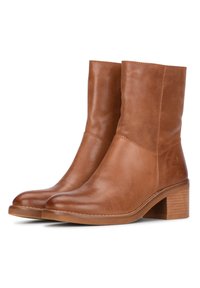 Botines de cuero marrón con puntera redondeada, textura suave y tacón apilado. Detalle de costura mínima, presenta un diseño sencillo.