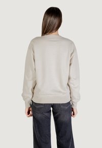Sudadera beige con cuello redondo, corte relajado, puños y dobladillo acanalados, combinada con jeans gris oscuro, vista desde la parte posterior.