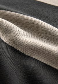 Struktureret stof med vandrette striber i mørkegrå og beige. Det strikkede materiale virker blødt, med synlige vævemønstre og dybde.