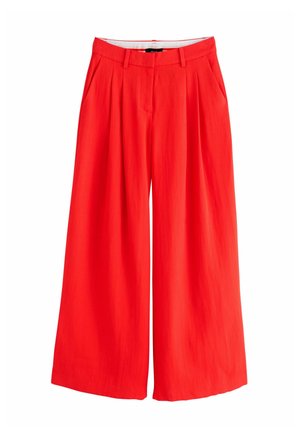 Witte mouwloze top ingestopt in een hooggetailleerde, geplooide rode broek met riemlussen en zijzakken, gedragen door een persoon.