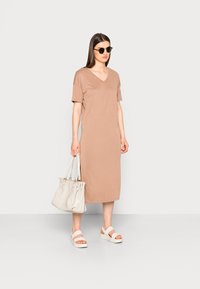 Vestido bege até ao joelho com decote em V e mangas curtas, combinado com uma bolsa branca e sandálias brancas de sola grossa. Textura de tecido suave.