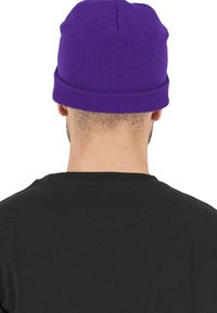 Berretto lavorato a maglia viola con bordo ripiegato, materiale testurizzato, cima arrotondata e finitura liscia, indossato con una maglietta nera.
