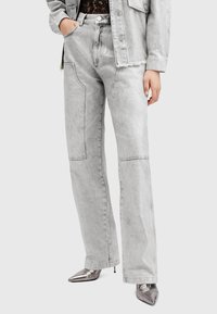 Jeans de pierna ancha gris claro con un acabado texturizado y detalles de costura visibles. Cuenta con bolsillos inclinados y un dobladillo deshilachado.