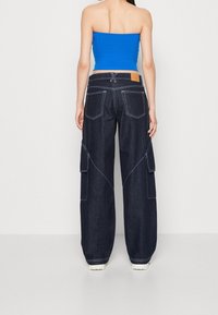 Mörkblå denim cargobyxor med vida ben, kontrasterande vita sömmar, stora sidofickor och en etikett på baksidan av midjan.
