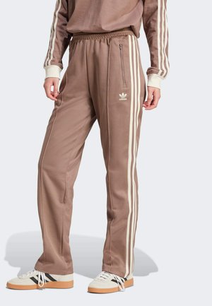 Pantaloni sportivi marroni realizzati in tessuto morbido, con strisce laterali bianche e una fascia elastica in vita con una tasca con zip. Decorati con un piccolo logo.