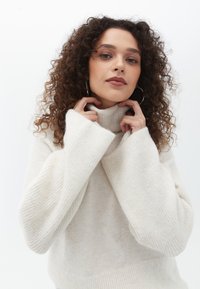 Cremfarbener, gestrickter Pullover mit hohem Kragen, gerippten Ärmeln und weicher Textur. Das Design zeichnet sich durch übergroße Ärmel und eine lockere Passform aus.