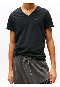 Black cotton v-neck t-shirt featuring a small logo on the chest; paired with gray sweatpants that have a drawstring waist.