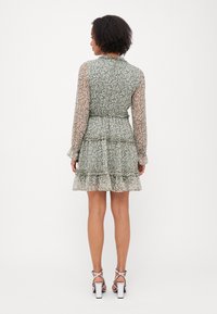 Green floral-patterned dress with long sheer sleeves, ruffled tiers, and a fitted waist. The fabric has a soft texture and layered design.