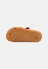 Barefoot sandal with a flexible tan rubber sole, featuring a textured surface and a pink fabric strap. Printed logo on the sole.