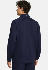 Sudadera atlética de mangas largas en azul marino con un alto cuello, mangas tipo raglán y un pequeño logotipo en la parte posterior. Fabricado en tejido suave y ligero.