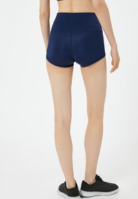 Pantalones cortos deportivos de color azul marino con una cintura alta, con una textura suave y un dobladillo redondeado. Llevados con zapatillas de correr negras.