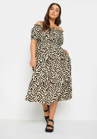 Abito maxi off-the-shoulder beige con stampa zebra marrone, vita elasticizzata e maniche a volant. Abbinato a sandali con platform neri.