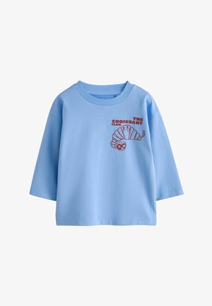 Hellblaues Langarmshirt mit rotem Grafikmotiv eines lächelnden Croissants, das einen karierten Becher hält, und dem Text „The Croissant Club“ auf der Brust.