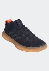 Scarpa sportiva nera con tomaia in mesh testurizzato, lacci e dettaglio delle tre strisce; presenta una suola in gomma flessibile e un linguetta arancione sul tallone.