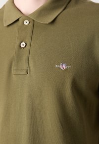 Olivengrøn polo-shirt lavet af tekstureret bomuld, med en tre-knap placket og broderet logo på venstre bryst.