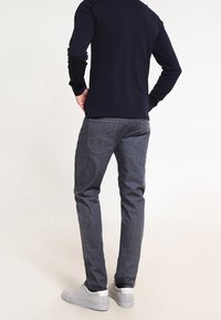 Grå jeans med slim fit, med bakfickor och en subtil tvätt, tillsammans med en marinblå långärmad topp och ljusgrå sneakers.