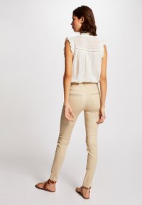 Witte blouse met ruches aan de mouwen, gecombineerd met strakke beige broek en bruine sandalen met versieringen. Gladde stof met een relaxte pasvorm.