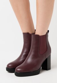 Bordowe botki za kostkę wykonane ze skóry, z elastycznymi bocznymi panelami, okrągłym noskiem, teksturowaną gumową podeszwą i słupkowym obcasem.