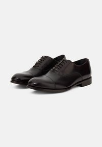 Scarpe eleganti in pelle nera con una finitura liscia, punta rotonda e design con punta rinforzata. Presentano sei occhielli per lacci e un tacco basso.