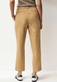 Khaki trousers with a straight leg design, back pockets, and a mid-rise waist, paired with white sneakers featuring black accents.
